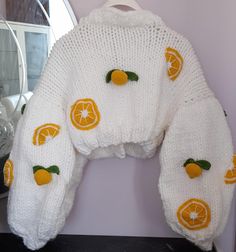 a white sweater with oranges on it is hanging from a hook in front of a mirror