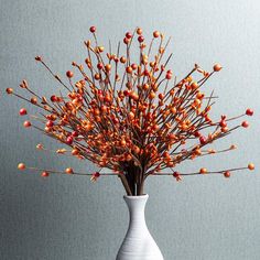 a white vase filled with red berries on top of a wooden table next to a gray wall