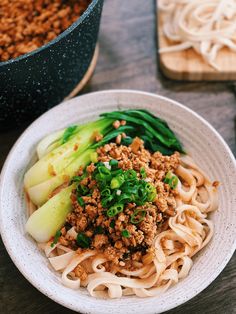 a white plate topped with noodles and meat next to a pot of broccoli