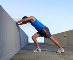 a man is leaning against a wall and stretching his arm on the side while wearing running shoes