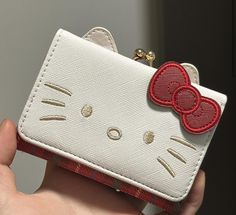 a hand holding a white hello kitty wallet