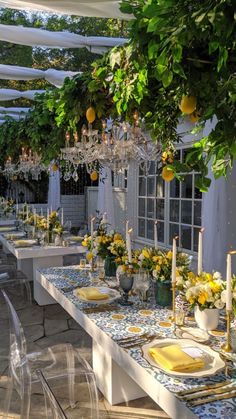 an outdoor dining area with yellow flowers and lemons on the table, chandelier hanging from the ceiling