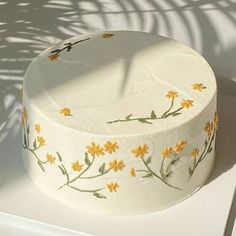 a white cake with yellow flowers painted on it's side sitting on a table