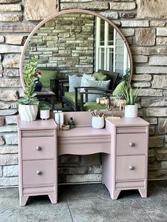 a pink vanity with mirror and potted plants in front of a brick wall,