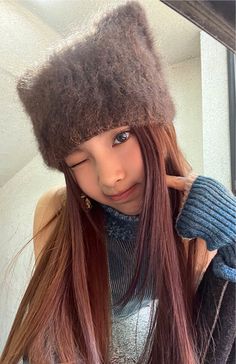 a girl with long red hair wearing a hat and mittens looking at her reflection in a mirror