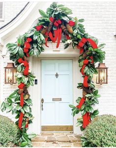 a christmas wreath on the front door of a white house with red ribbon and pine cones