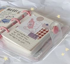 an open notebook with writing on the pages and pink ribbon attached to it, sitting on a clear plastic tray