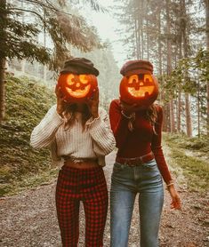 two girls wearing pumpkin heads walking down a path in the woods with jack - o'- lanterns on their faces