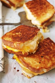 two grilled cheese sandwiches sitting on top of a piece of paper next to a knife