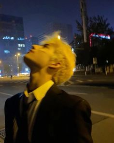 a man with blonde hair standing in the street at night