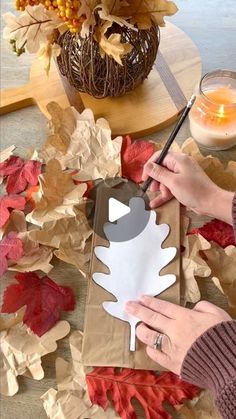 a woman is making a paper cutout with leaves on the ground and candles in the background