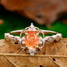 an orange and white diamond ring sitting on top of a leaf