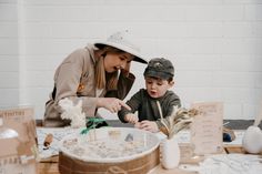 a woman is helping a young boy make crafts at a table with other items on it