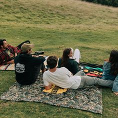 four people sitting on a blanket in the grass with their backs to each other and looking at something