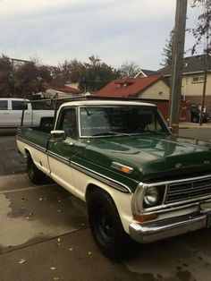 an old green and white pickup truck parked on the side of the road in front of some houses