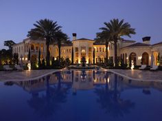 a large mansion with a swimming pool in front of it at night, surrounded by palm trees