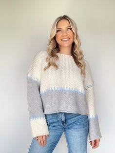 a woman wearing a sweater and jeans standing in front of a white wall with her hands on her hips