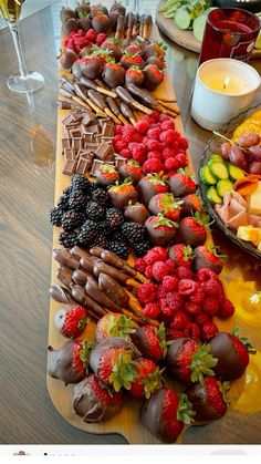 an assortment of fruits and chocolates arranged on a wooden platter with wine glasses in the background