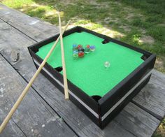 a pool table with two cues and three balls on it, sitting outside in the grass