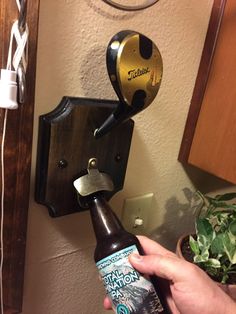 a person holding a beer bottle in front of a wall mounted hook on a wall