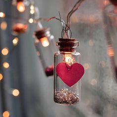 a mason jar with a heart hanging from it's side and some lights in the background