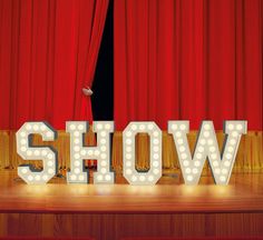 the word show is lit up in front of a red curtained stage with lights