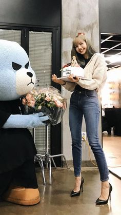 a woman standing next to a giant teddy bear holding flowers and a box of chocolates