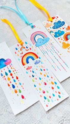 three bookmarks with rainbows, clouds, and hearts on them sitting on a table