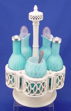 three blue glass vases sitting on top of a white stand with a toothbrush holder