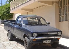 an old blue pick up truck parked on the side of a road next to a building