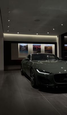 a car is parked in a showroom next to two large pictures on the wall