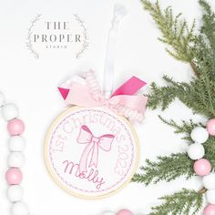 a cross stitch ornament with a pink bow on it next to some christmas decorations