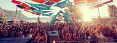 a large group of people standing around each other at a music festival with flags flying in the air