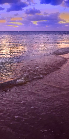 an ocean beach with waves coming in to shore and the sun setting on the horizon