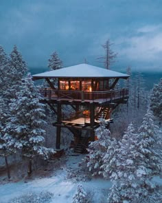 a tree house surrounded by snow covered trees in the woods at night with lights on