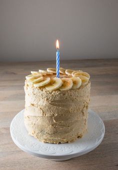 a cake with banana slices and a single candle on it sitting on a white plate