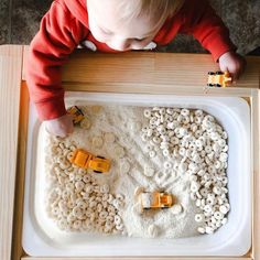 a toddler playing with legos in a play tray made out of white rice