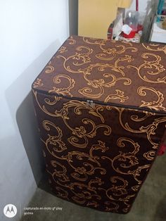 a brown and gold patterned box sitting on top of a floor next to a wall