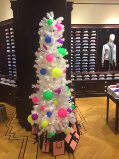 a white christmas tree with colorful balls and tags on it in front of a store display