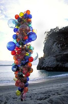 a bunch of balloons that are in the air on a beach with water and rocks