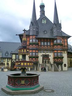 a large building with two towers and a fountain in front of it on a cobblestone street