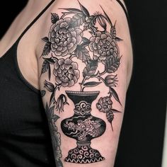 a woman's arm with flowers and vase tattoo on her left upper half sleeve