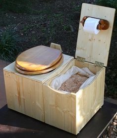 an open toilet sitting on top of a wooden box next to a trash can and grass