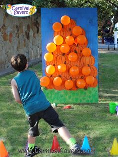 a young boy standing in front of an orange tree made out of plastic cups and cones