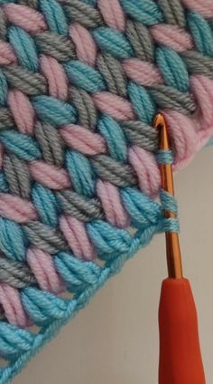 an orange crochet hook next to a blue and pink knitted blanket