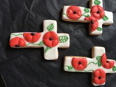 three decorated cookies with red flowers and green leaves on black paper next to each other