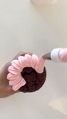 a person is holding a cupcake with pink frosting on it and a toothbrush in their hand