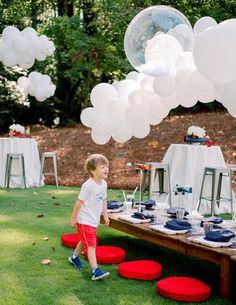 a little boy standing in front of a table with balloons and plates on top of it