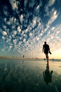 a man is walking on the beach with his surfboard in hand and clouds in the sky