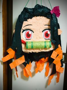 a paper mache with red eyes and green hair is hanging on the wall next to orange pieces of tape